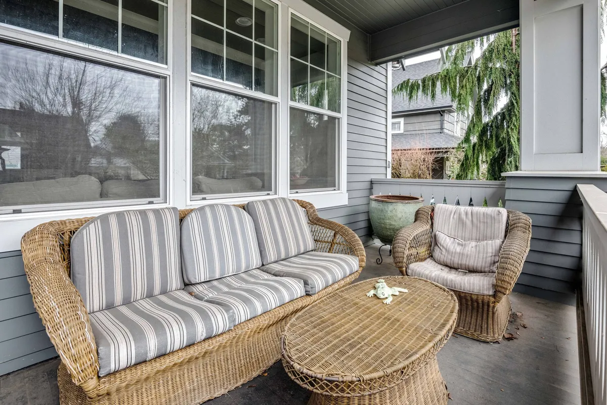 A sunlit sitting area with wicker sofa and chair, coffee table, and expansive windows that offer an abundance of natural light. The setting is relaxed and comfortable, ideal for casual chats or unwinding after a work session.