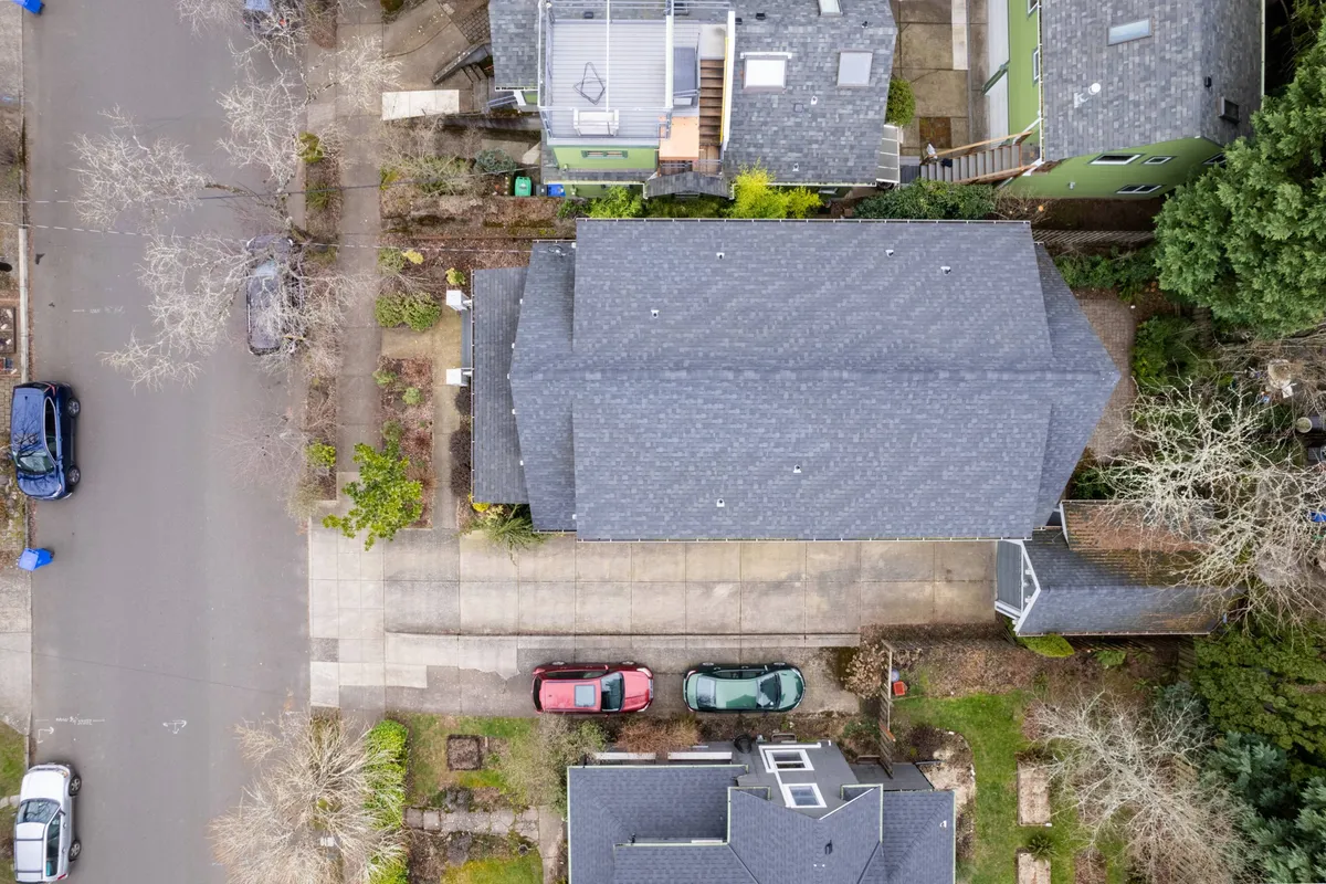 A serene view of neighborhood rooftops, leafy streets, and driveways offers context for the home's location. The peaceful, community-oriented vibe depicted is ideal for families embarking on walks, bike rides, or gatherings after park outings. The lush greenery and open space reinforce the 'explore' narrative.