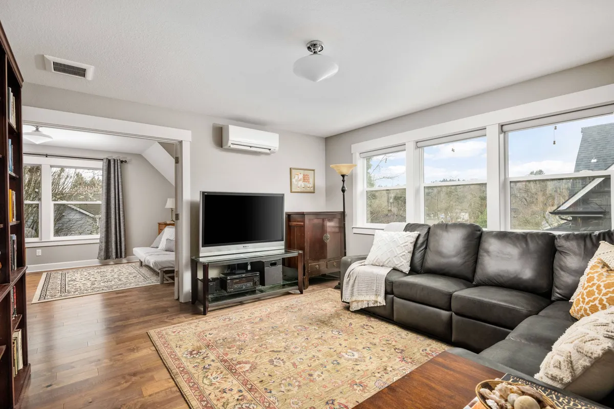 A welcoming media room featuring a large leather sofa positioned for prime views of a wall-mounted television. The space is accented by a decorative rug, plentiful window light, and thoughtful touches that encourage relaxation and togetherness.