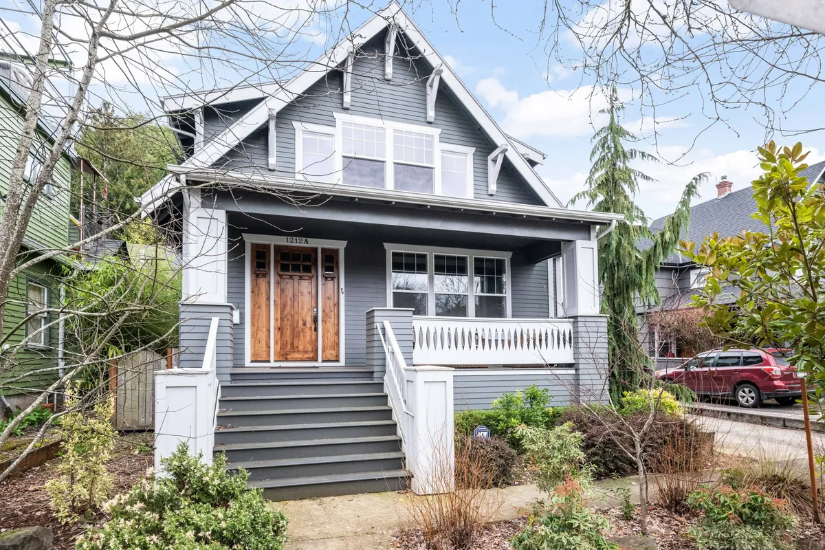 A wide view of the home's welcoming front porch featuring comfortable seating and a stylish exterior door. There is ample space for enjoying a morning coffee or relaxing in the evening. The porch is accented with windows and slight garden touches, illustrating the inviting, community-oriented vibe mentioned in the section.