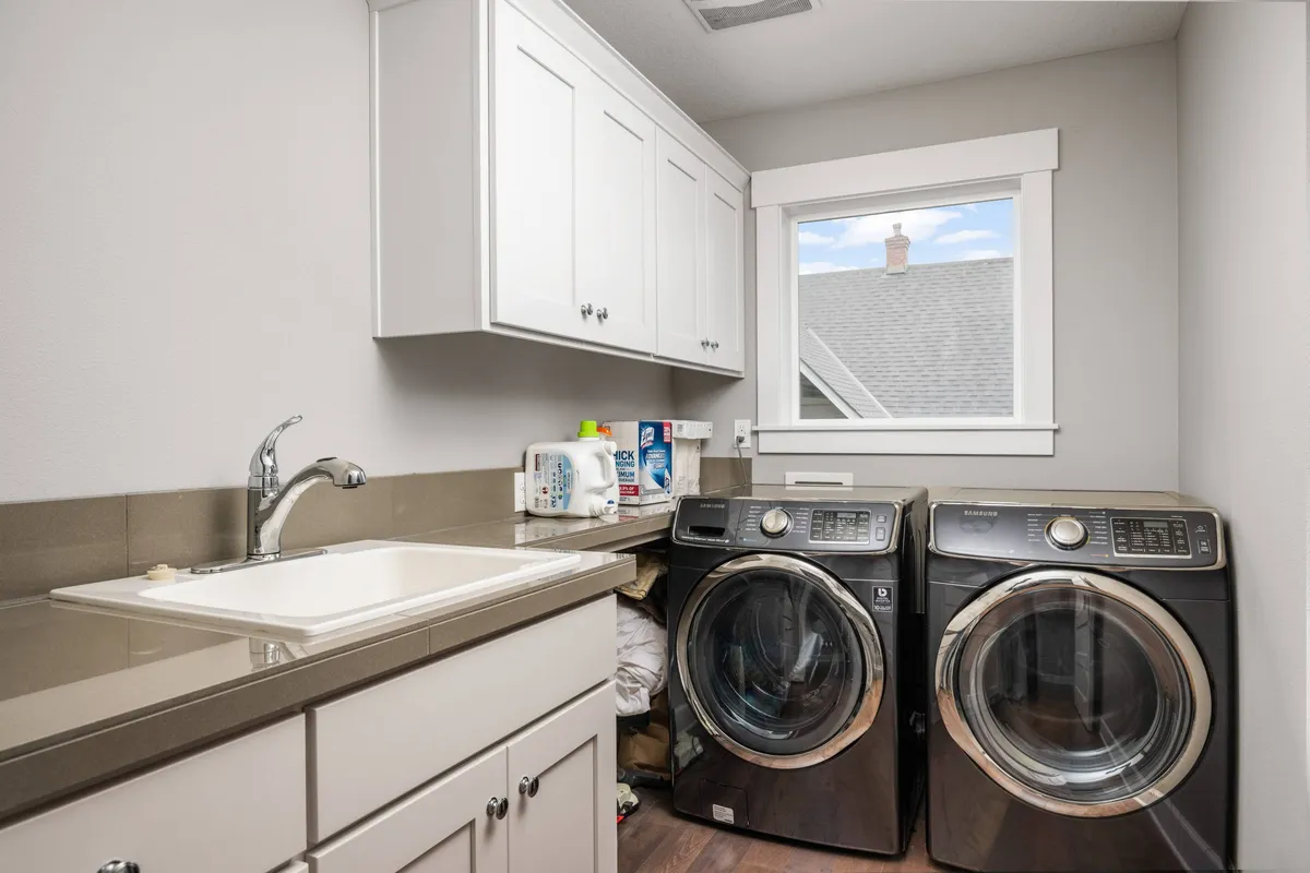 A compact, practical laundry area with a washer and dryer stacked efficiently beside a utility sink. A window lets in natural light, making the space feel fresh and functional.